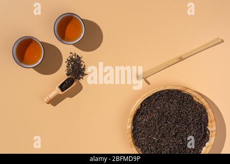 Gebrauter schwarzer Puer-Tee in Keramikschalen, trockene pu-erh-Teeblätter in einem hölzernen Bambusplatte auf beigem Hintergrund, Teezeremonie Stockfoto