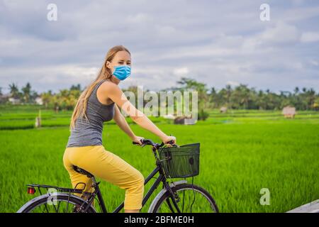 Eine junge Frau in medizinischer Maske fährt auf einem Reisfeld in Ubud, Bali, mit dem Fahrrad. Bali Travel Concept Touristen fürchten das 2019-ncov Virus. Medizinische Maskierung Stockfoto