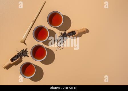 Schwarzer Puer Tee in Keramikschalen, trockene pu-erh Teeblätter in einem hölzernen Bambuslöffel auf einem beigen Hintergrund, Tee Zeremonie Minimalismus Stockfoto