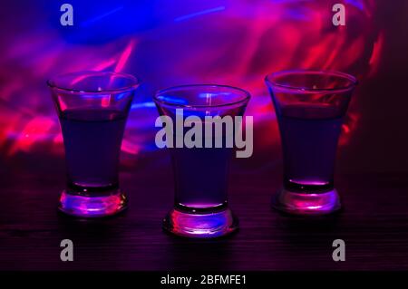 Drei Drinks auf der Party. Drei Aufnahmen mit Cocktails an der Bar. Spirituosen, Wodka, frisch. Leuchtet auf einem farbigen Hintergrund. Nachtclub, nach der Party. Stockfoto