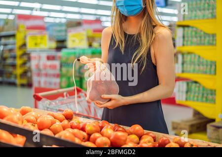Eine Frau wählt Tomaten in einem Supermarkt ohne Plastikbeutel. Wiederverwendbare Tasche für den Kauf von Gemüse. Konzept ohne Verschwendung Stockfoto