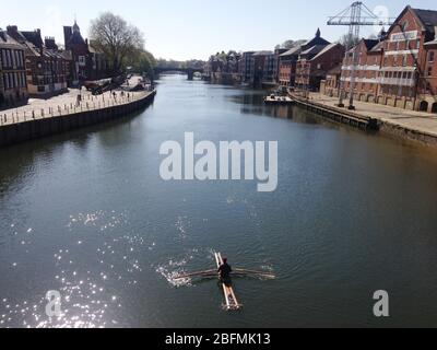 Ein Mann isoliert sich selbst, während er sein selbstgebautes Boot auf seiner Jungfernfahrt durch den Fluss Ouse im Stadtzentrum von York reiht. Stockfoto