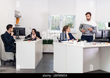 Ein multirassisches Team, das an Computern arbeitet, kommuniziert und in einem Coworking Space kooperiert. Stockfoto