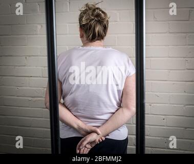 Eine weibliche Gefangene hinter Gittern in einem Frauengefängnis. Bild nach Modell gestellt. Stockfoto