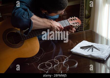 Mann im Hemd bereitet und ändert die Saiten einer spanischen Gitarre zu Hause in der Nähe eines Fensters. Holztisch mit neuen Saiten in klassischen Indoor-Platz. Stockfoto