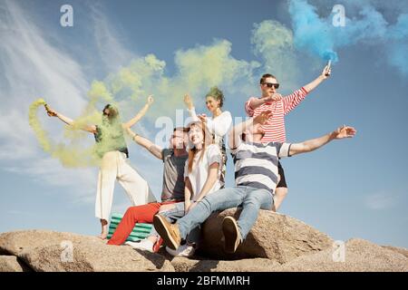 Gruppe von stilvollen jungen Menschen sitzen auf Felsen mit Rauchgranaten und genießen schönen Sommertag, niedrigen Winkel Blick Stockfoto