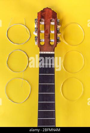 Ändern der Saiten zu einer Gitarre: Gitarrenhals ohne Saiten und neue Saiten auf dem Instrument isoliert auf gelbem Hintergrund setzen. Die Arbeit der Geigenbauer. Stockfoto