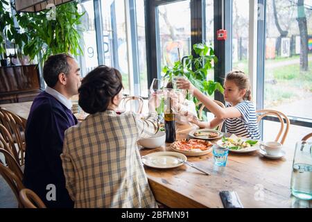 Eine vierköpfige Familie, die beim Abendessen in einem Café Gläser aufhebt. Stockfoto