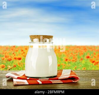 Glas Milch auf Holztisch vor Mohnblumen und blauem Himmel Hintergrund Stockfoto