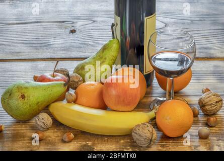 Ein Glas und eine Flasche Fruchtwein und gemischtes Obst neben dem Tisch Stockfoto