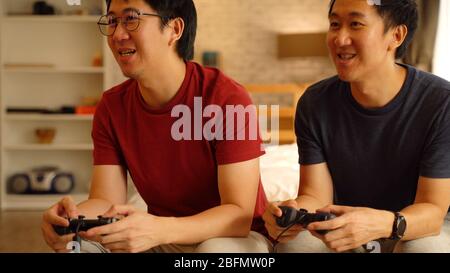 Junge männliche Freunde spielen Spiel mit Joystick zu Hause. Asiatische Männer Fernsehen Videospiel zusammen zu spielen. Stockfoto