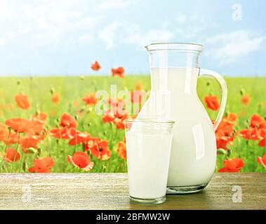 Krug, Glas Milch auf Holztisch gegen Mohnblumen und blauer Himmel Hintergrund Stockfoto