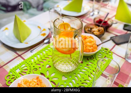 Grüne Servietten auf Tellern in Dreiecksform angeordnet, Limonade aus Wasser und Orangenscheiben in einem großen Krug, Salate sichtbar. Stockfoto