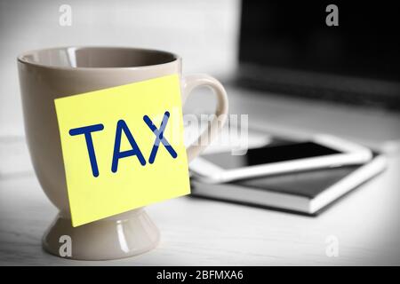 Steuerkonzept. Gelbe Haftnotiz auf Kaffeetasse, auf Laptop-Hintergrund Stockfoto