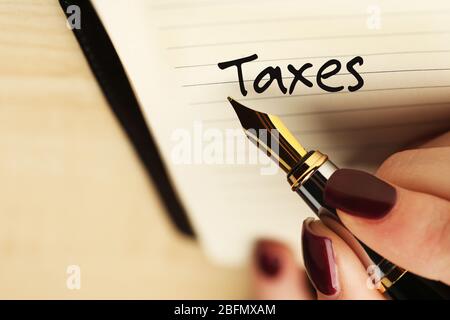 Steuerkonzept. Weibliche Hand Schreiben Steuern von Stift auf Holztisch Hintergrund Stockfoto