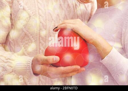 Weibliche und männliche Hände halten rotes Herz auf verschwommenem Hintergrund. Familie, Liebe und Gesundheitskonzept Stockfoto