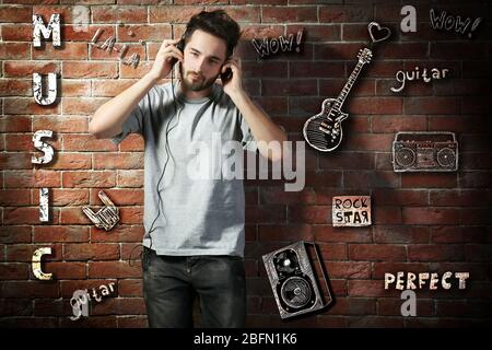 Junger Mann mit Kopfhörern, der Musik auf Backstein-Hintergrund hört Stockfoto