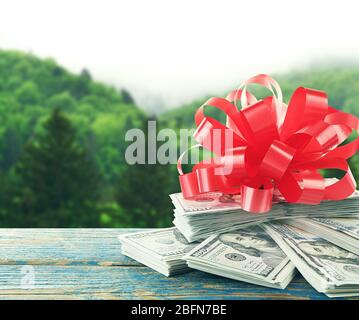 Dollarstapel mit Bogen als Geschenk auf Naturhintergrund Stockfoto