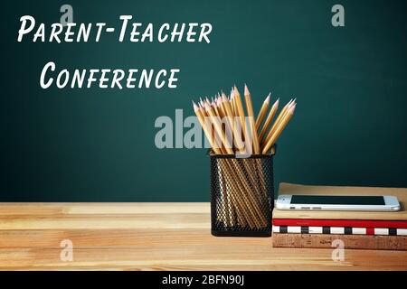 Stationär und Smartphone auf Holztisch. Text ELTERN-LEHRER-KONFERENZ auf Tafel Hintergrund. Schulkonzept. Stockfoto