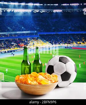 Bier mit Snack und Ball auf dem Tisch vor Fußballfeld Hintergrund. Sport- und Unterhaltungskonzept. Stockfoto