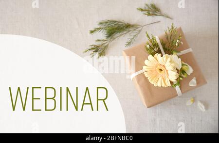 Geschenkbox mit Blumen und Wort WEBINAR auf textilen Hintergrund verziert. Floristin und Blumendesign Tutorial Konzept. Stockfoto