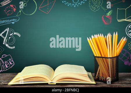 Buch mit Bleistiften im Halter auf dem Tisch. Kreative Skizzen auf dem Hintergrund der Tafel. Kinderentwicklungskonzept. Stockfoto