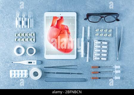 Tablet mit medizinischen Geräten auf farbigem Hintergrund. Herz auf dem Bildschirm. Medizin und modernes Technologiekonzept. Stockfoto