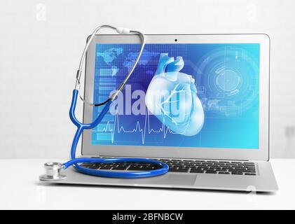Laptop mit Stethoskop auf dem Tisch. Herz auf dem Bildschirm. Medizin und modernes Technologiekonzept. Stockfoto
