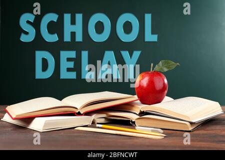 Bücher und Apfel auf Tafel Hintergrund mit Text SCHULE VERZÖGERUNG Stockfoto