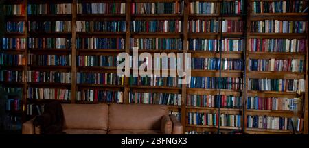 Bücherregale in der Bibliothek. Buchhintergrund. Großes Bücherregal mit vielen Büchern. Sofa im Zimmer zum Lesen von Büchern. Bibliothek oder Shop mit Bücherregal. Stockfoto