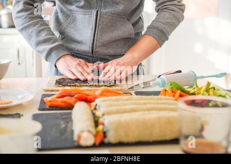 Kaukasischer Mann bereitet hausgemachte Sushi-Rollen. Sushi Formen. Die Schritte zum Erstellen von Sushi mit Lachs. Prozess der Sushi-Herstellung durch Nachkochen auf Stockfoto