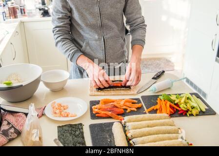 Kaukasischer Mann bereitet hausgemachte Sushi-Rollen. Sushi füllen. Die Schritte zum Erstellen von Sushi mit Lachs. Prozess der Sushi-Herstellung durch Nachkochen auf Stockfoto