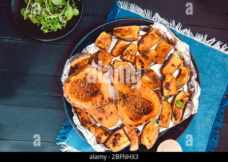 Draufsicht gebacken geröstet gegrillte ganze orange Kürbis Butternut Kürbis Halbtöne und Süßkartoffel-Dias mit Kräutern auf dem Backblech auf blauer Serviette und b Stockfoto