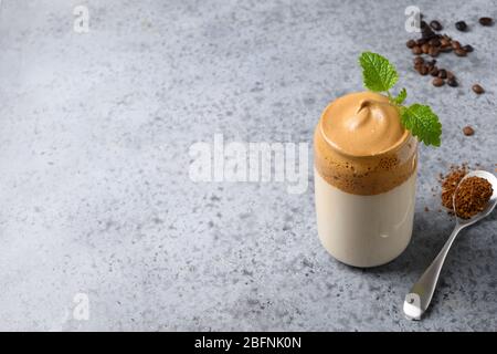 Dalgona schaumiriger Kaffee im Glas garnieren melissa auf grau. Trend koreanischen Eisgetränk mit Schaum von Instant-Kaffee. Nahaufnahme. Kopierbereich. Stockfoto