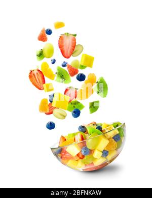 In Scheiben geschnittene Früchte fallen in Schüssel mit Salat auf weißem Hintergrund Stockfoto