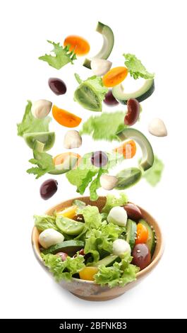 Geschnittenes Gemüse fällt in Schüssel mit Salat auf weißem Hintergrund Stockfoto
