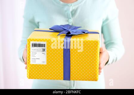 Frau hält Paket Geschenk-Box mit Tracking-Code auf hellem Hintergrund Stockfoto