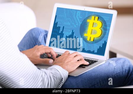 Mann, der Laptop mit Bitcoin-Symbol auf dem Bildschirm zu Hause Stockfoto