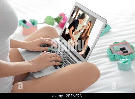 Frau sitzt auf dem Bett mit Laptop und beobachten Online-Training für professionelle Make-up-Künstler Stockfoto