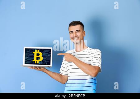 Mann, der Laptop mit Bitcoin-Symbol auf dem Bildschirm vor farbigem Hintergrund hält Stockfoto