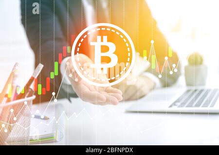 Geschäftsmann mit virtuellem Bitcoin-Symbol am Tisch im Büro Stockfoto