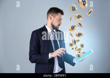 Geschäftsmann mit Tablet und Bitcoins auf hellem Hintergrund Stockfoto