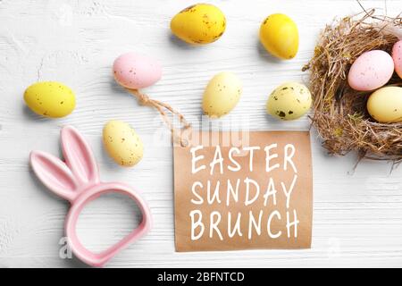 Text OSTERSONNTAG BRUNCH auf Karte. Bunte Eier auf weißem Holzhintergrund Stockfoto
