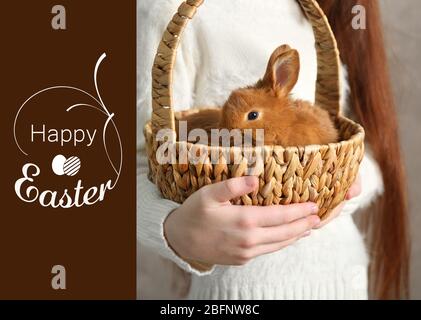 Mädchen mit Kaninchen in Weidenkorb und Text HAPPY EASTER auf Hintergrund Stockfoto