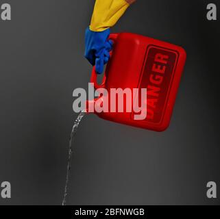 Konzept der Umweltverschmutzung. Hand gießt giftiges Wasser aus der Dose vor dunklem Hintergrund Stockfoto