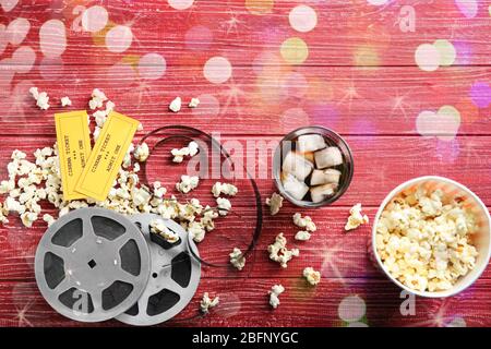 Flache Komposition mit Popcorn, Filmstreifen und unscharfen Lichtern auf Holzhintergrund. Kinoabend Stockfoto