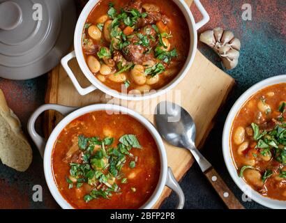 Bohnensuppe mit Fleisch und Gemüse auf einem rustikalen Brett mit Knoblauch serviert. Traditionelle Balkan-Suppe oder Eintopf Corbast Pasulj (Grah) Stockfoto