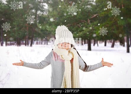 Verwirrt kleines Mädchen in einem trendigen gestrickte Kleidung und Schneeflocken auf Winter Park Landschaft Hintergrund Stockfoto