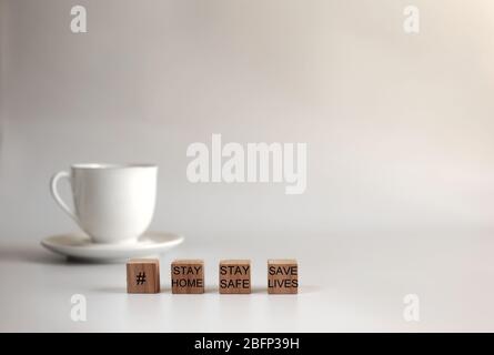 Konzept Bild ein Holzblock und Worte ZU HAUSE bleiben, SICHER bleiben, LEBEN retten mit weißen Tasse Kaffee auf weißem Hintergrund Stockfoto