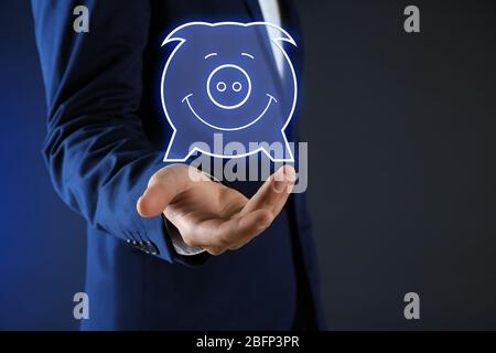 Geschäftsmann hält virtuelle Sparschwein auf dunklem Hintergrund Stockfoto